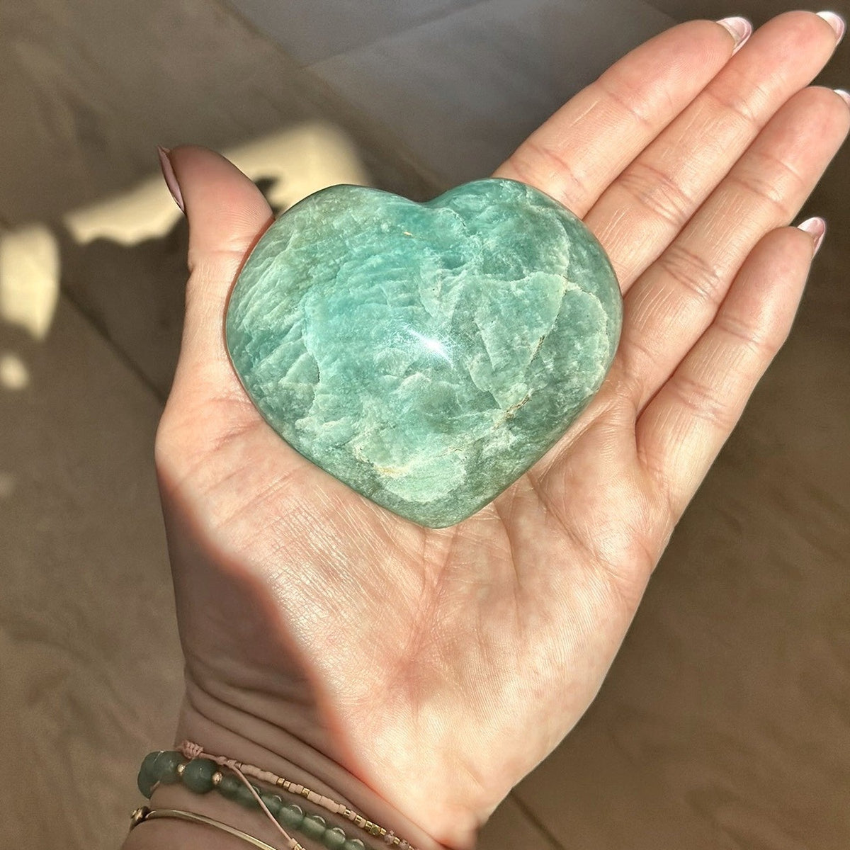 Hand-carved heart of soft teal amazonite held in the palm