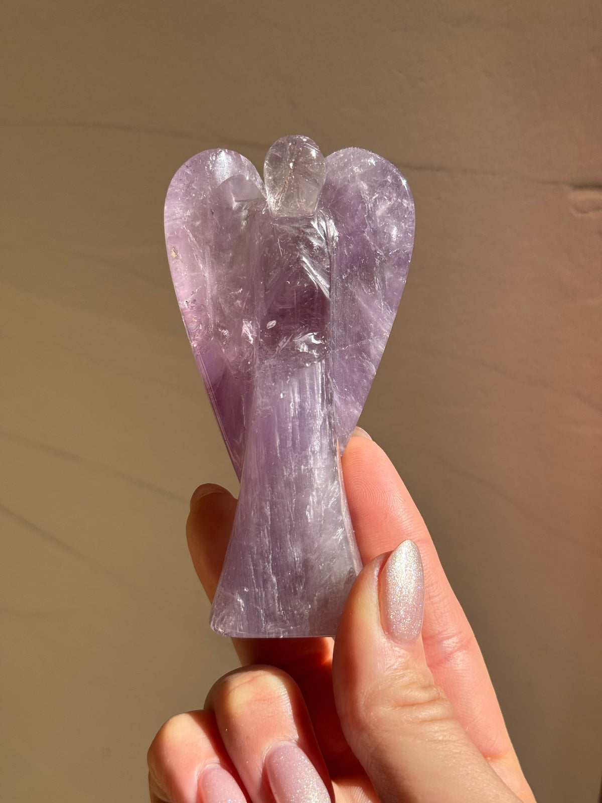Hand-carved lavender amethyst angel held up in the sunlight
