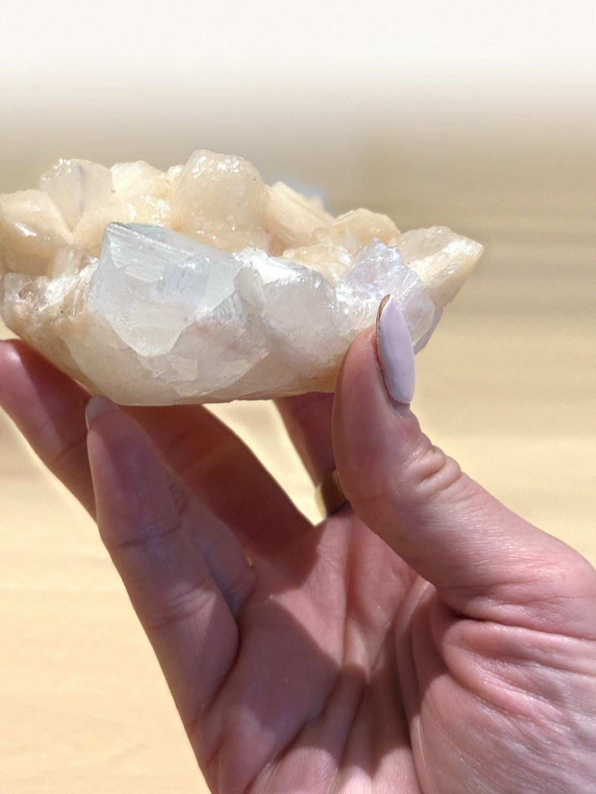 The apophyllite and peach stilbite cluster held in the hand to show its size