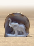 A blue chalcedony carving of an elephant with its trunk raised, standing in an arch of natural stone rind