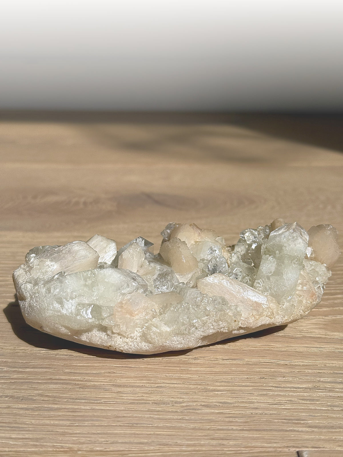 Green apophyllite and peach stilbite cluster on a wooden table