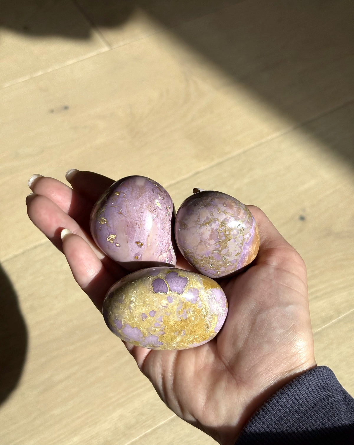 Three phosphosiderite meditation stones in lilac and gold, held in the hand