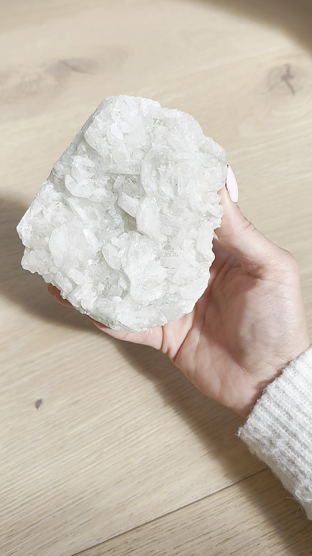 Snow-white apophyllite cluster held in the hand over a wooden floor